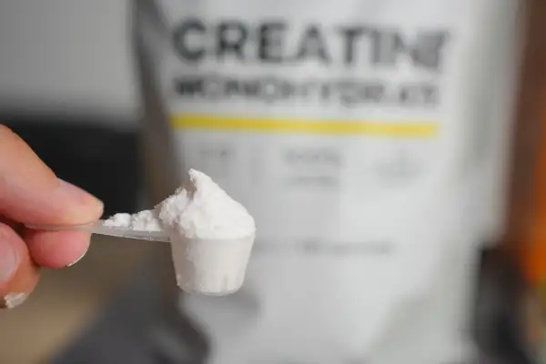 Heaped,Scoop,Of,Creatine,Powder,With,Bag,In,Background