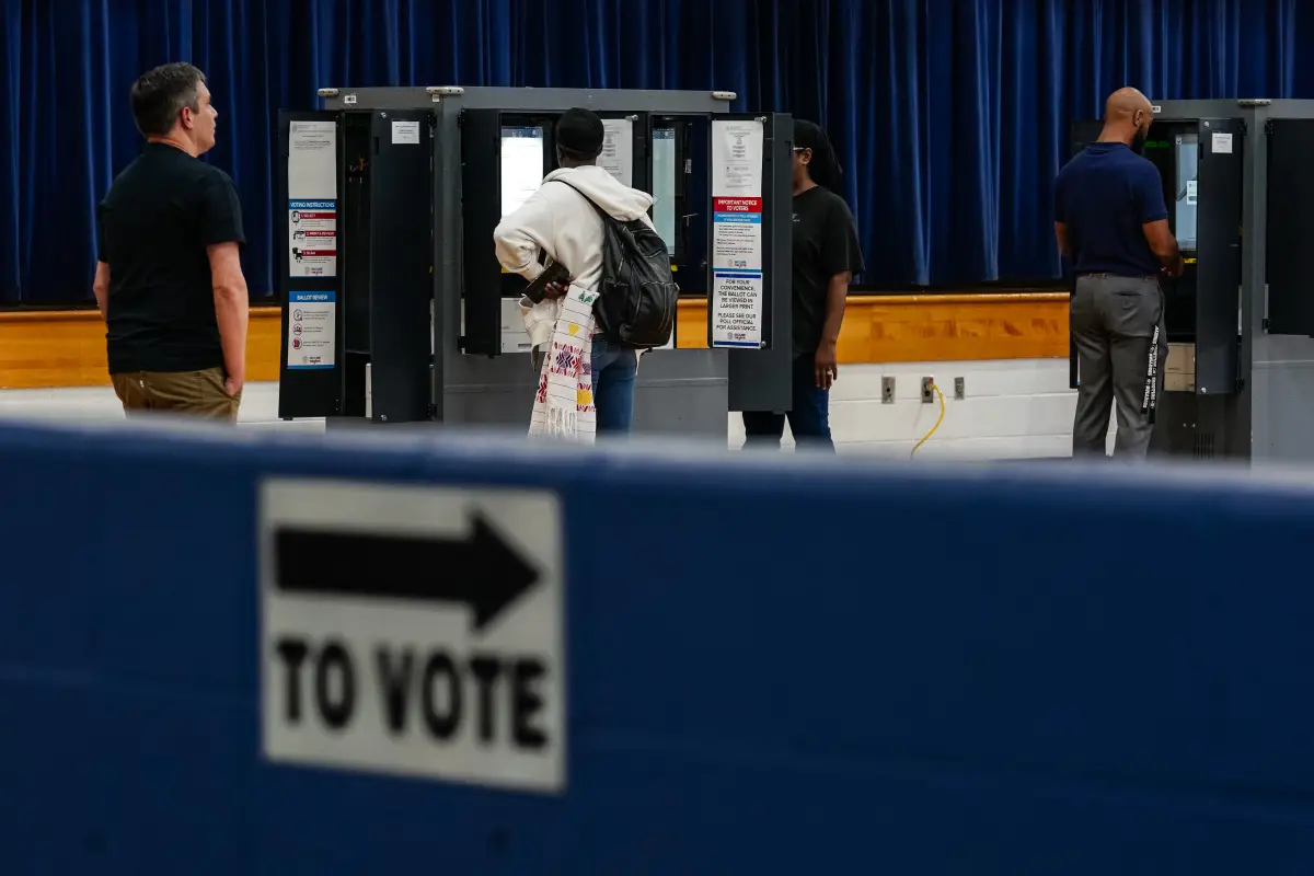 Se muestra a 4 personas formadas en el registro de votación para las elecciones presidenciales dentro de un auditorio.