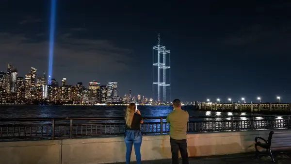 Personas observan y toman fotografías mientras un espectáculo de luces con drones que recrea las Torres Gemelas aparece en el horizonte durante las pruebas de la instalación "Tribute in Light" (Tributo en Luz) en el Bajo Manhattan, el 9 de septiembre de 2026, visto desde el Liberty State Park en Jersey City, Nueva Jersey. 