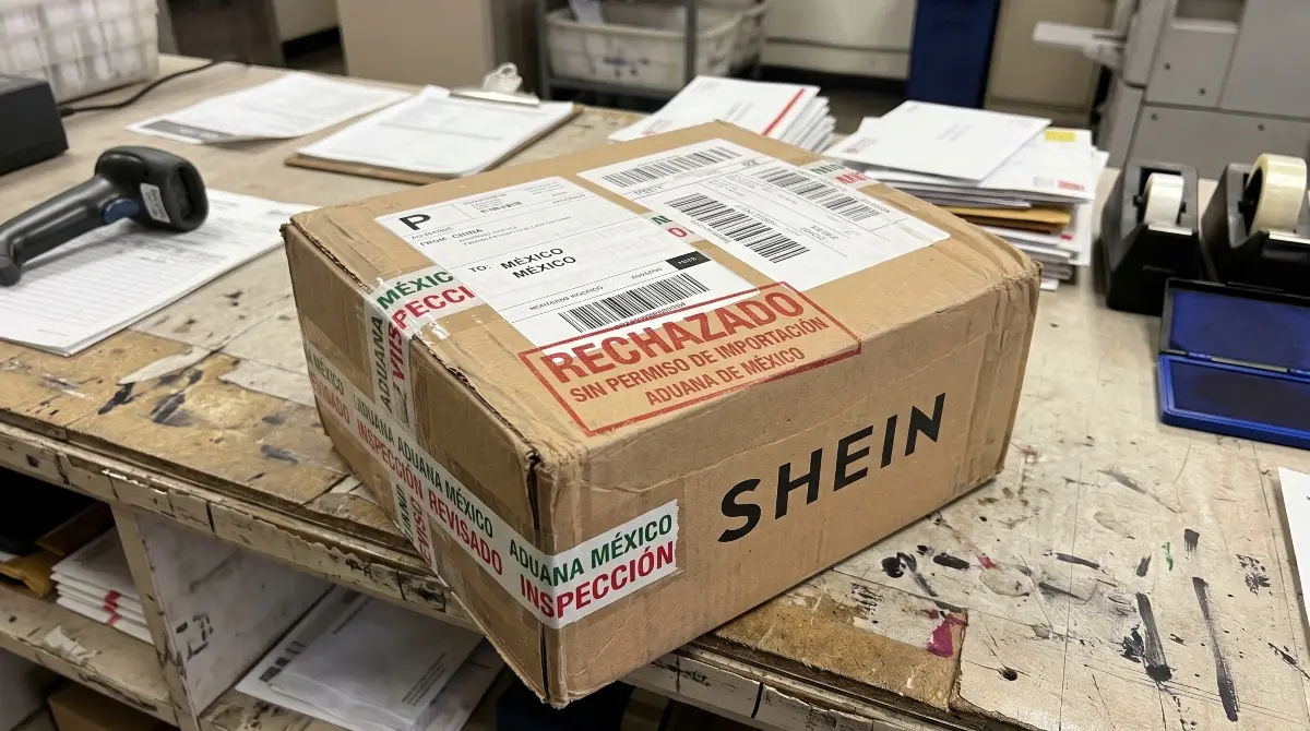 Una caja de cartón con el logo de Shein, con un sello que dice rechazado, sin permiso de importación de aduana, sobre una mesa de una oficina de paquetería. 