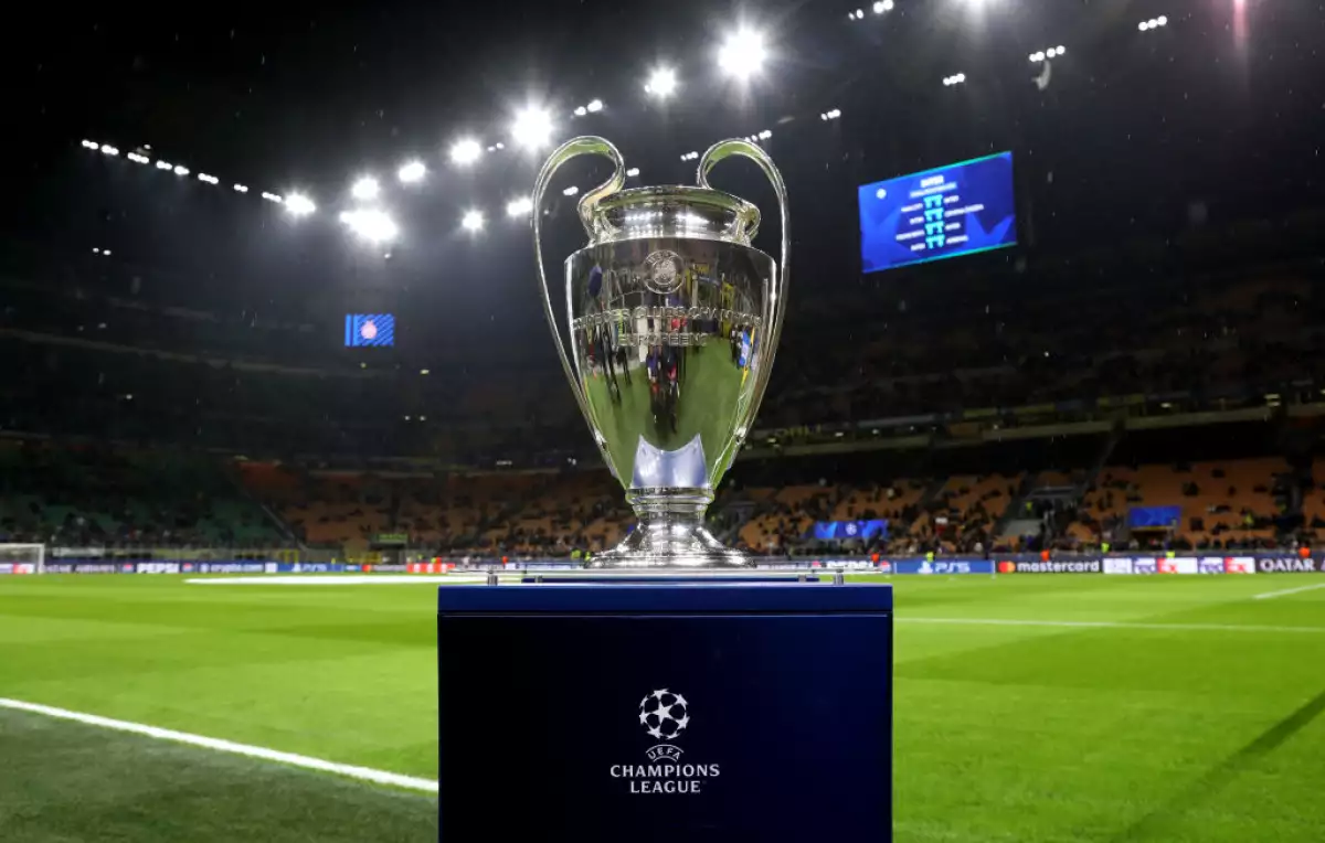 Foto del trofeo de la UEFA Champions League sobre su pedestal con un estadio lleno detrás.