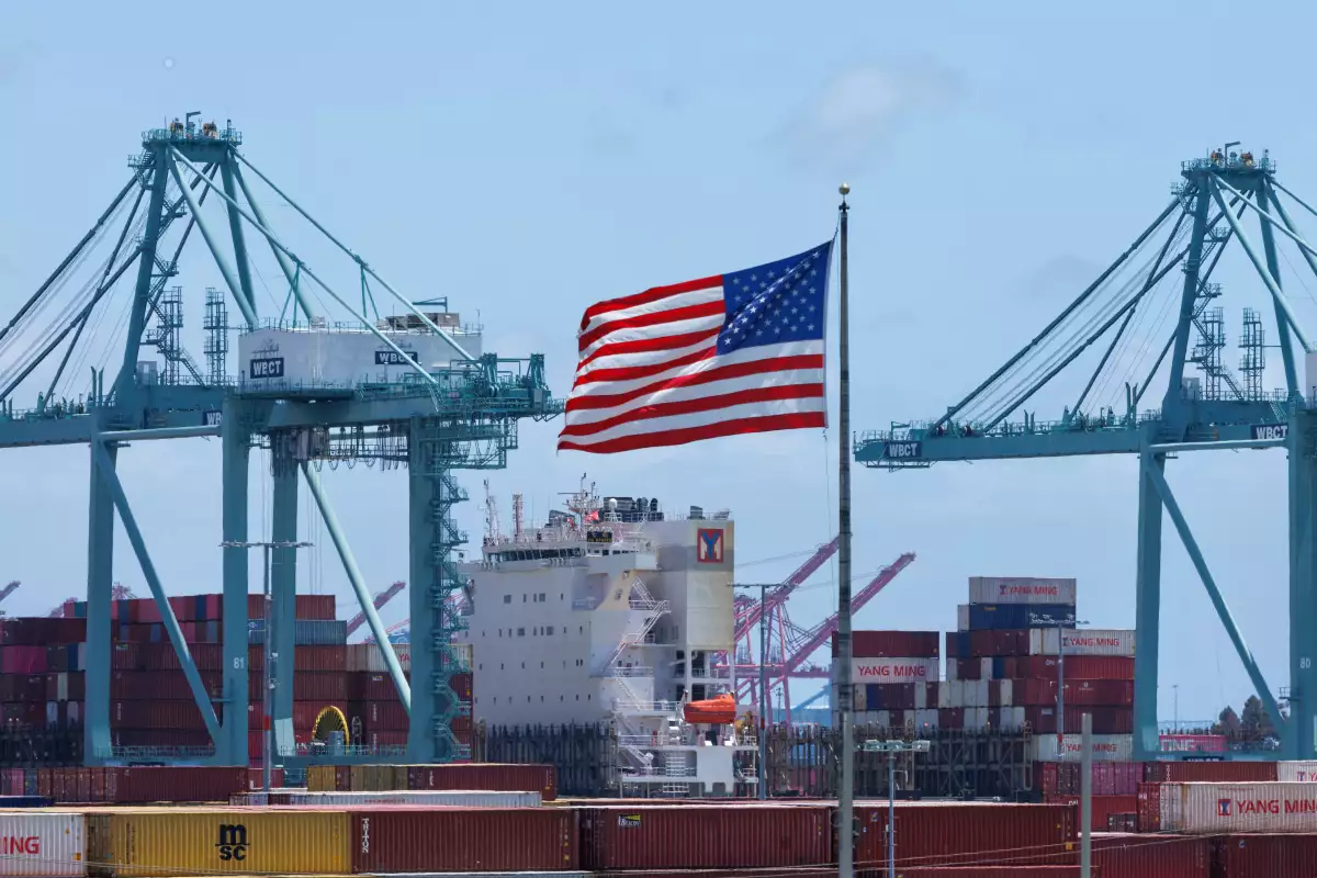 Una bandera estadounidense ondea cerca de los contenedores de envío mientras un barco es descargado en el puerto de Los Ángeles, en San Pedro, California, EE. UU., 1 de mayo de 2025.