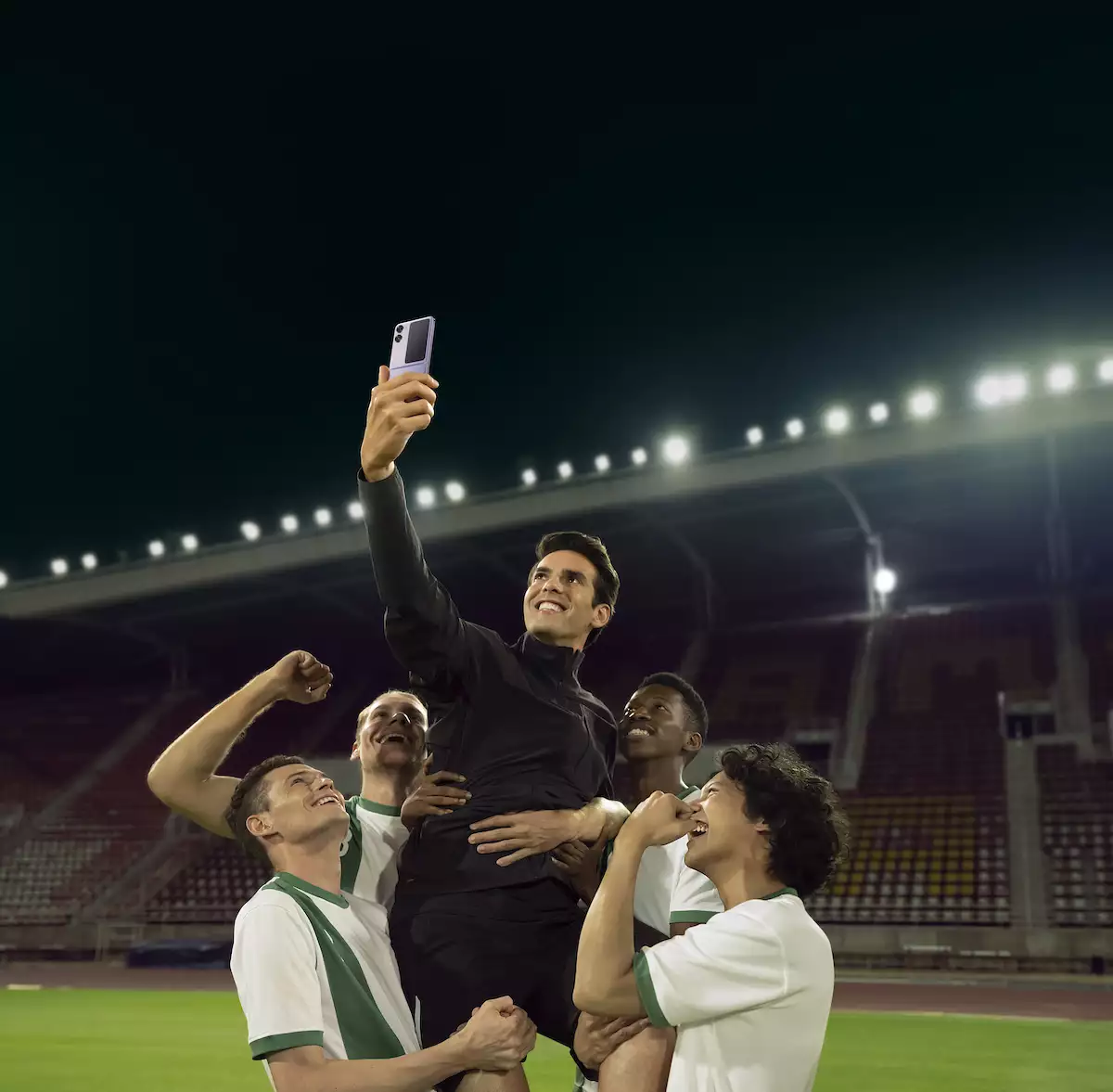 Imagen de jugadores de futbol cargando en hombros a Kaká mientras él se toma una selfie con su OPPO Find N2 Flip.