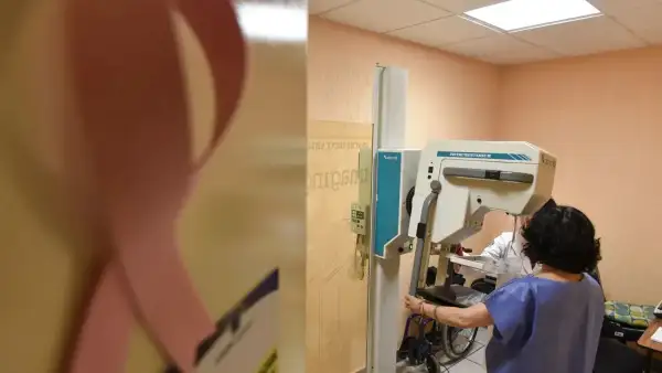 Consultorio médico, se ve un listón rosa representativo de la concientización de cáncer de mama y una persona se realiza una mastografía.