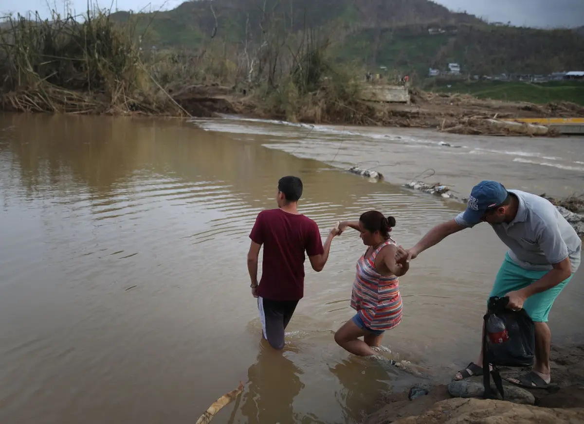 Héctor Ojeda, Sonia Robles y Tony Ojeda se preparan para cruzar un río a pie después de que el puente fuera arrastrado cuando el huracán María pasó el 27 de septiembre de 2017 en Morovis, Puerto Rico. Puerto Rico sufrió daños generalizados y graves, incluyendo la mayoría de las redes eléctricas, de gas y de agua, así como la destrucción agrícola después de que pasara el huracán María, un huracán de categoría 4.