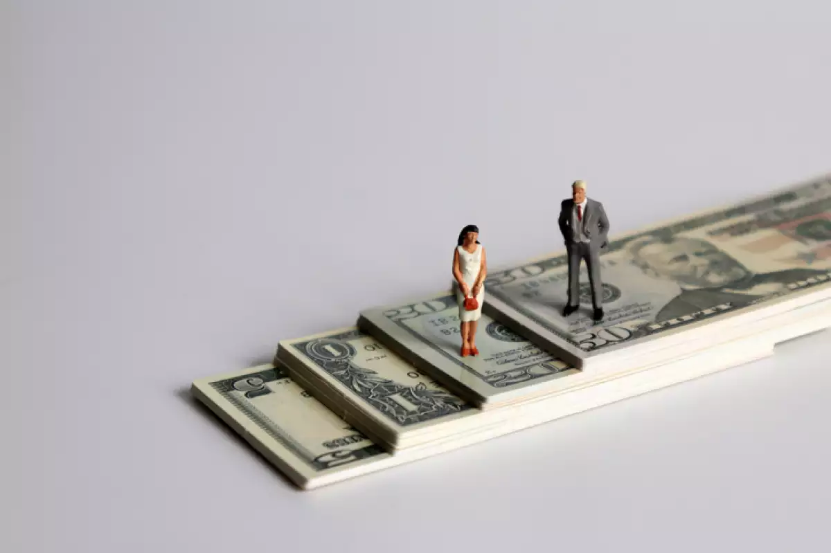 A miniature man and a miniature woman standing on a pile of bills.