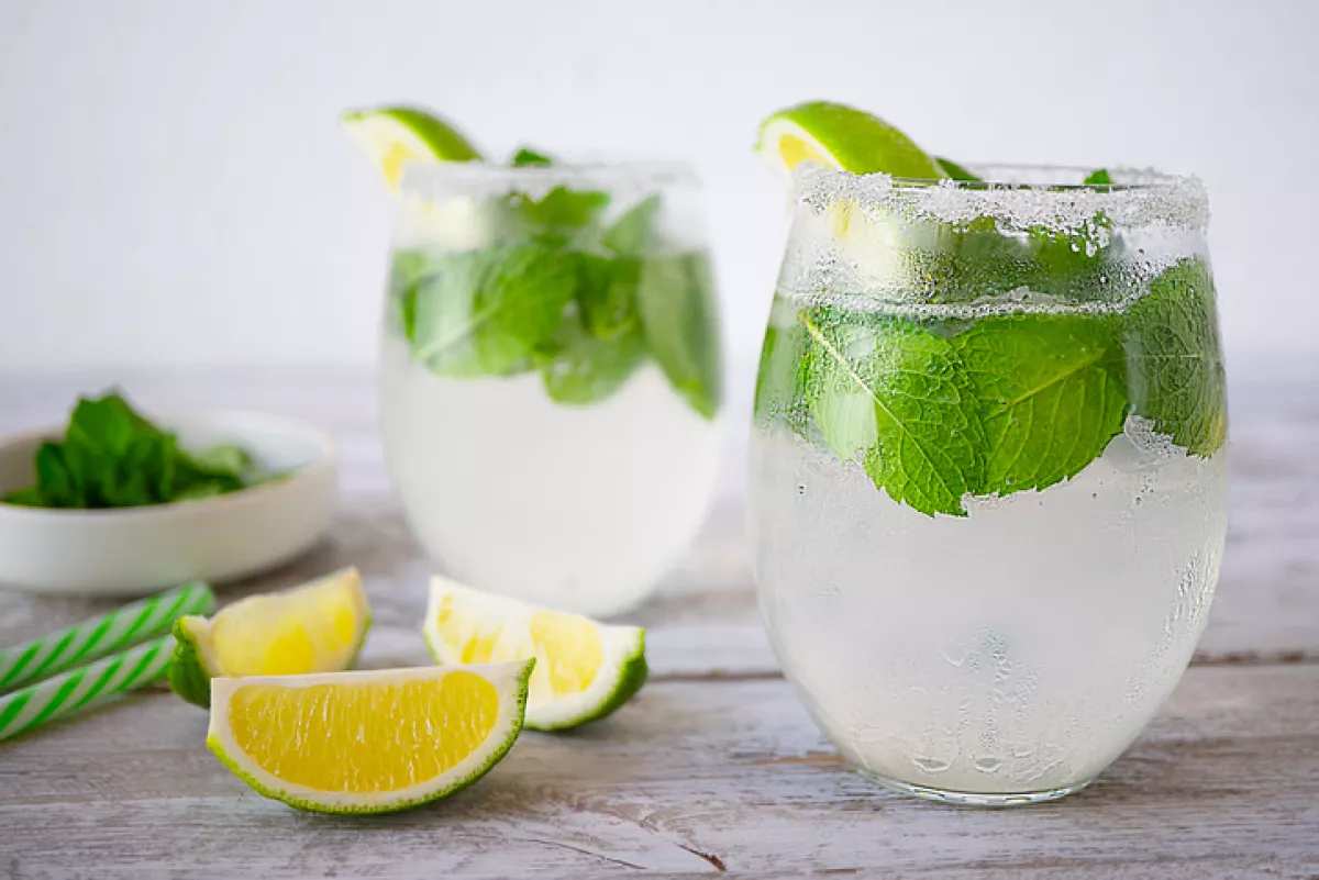 Dos vasos con rodajas de limón, popotes y plantas de menta.