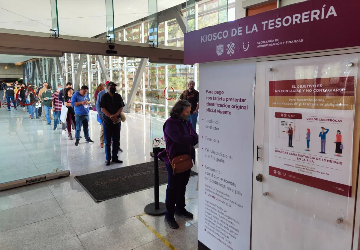 Personas formadas en una fila de un kiosco de la Tesorería de la CDMX. 