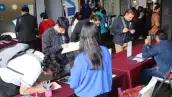 Un total de nueve jóvenes en una mesa roja llenando ofertas de empleo, una persona está sentada y con un papel en mano.jpg