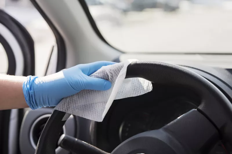 Hand with glove wiping car steering wheel.