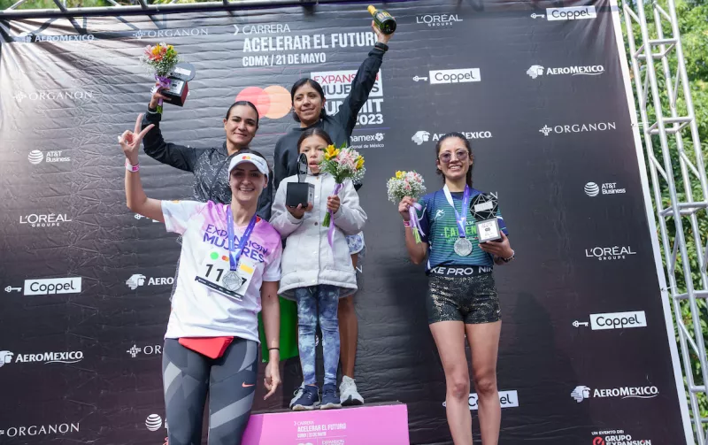 imagen de Michelle Romo, vicepresidenta de Mercadotecnia y Comunicaciones de MasterCard, celebrando en el podio con las ganadoras de la modalidad 10k de la Carrea Acelerar el Futuro.