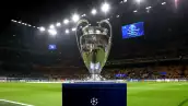 Foto del trofeo de la UEFA Champions League sobre su pedestal con un estadio lleno detrás.
