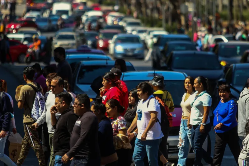 Personas cruzan una avenida frente a autos que esperan en la Ciudad de México.
