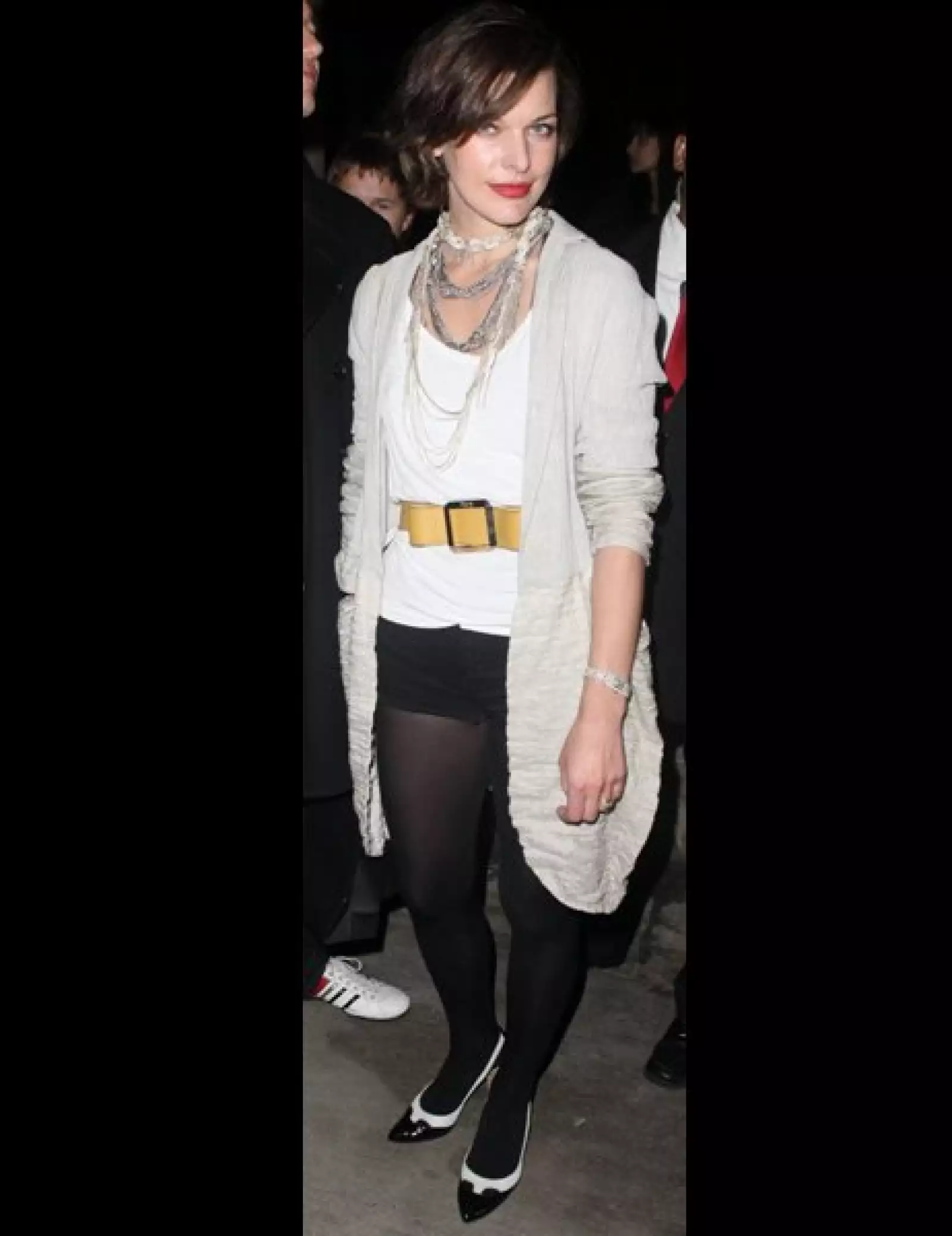 Milla Jovovich. Blusa blanca, shorts y medias negras para la noche, no olvidar el detalle de los zapatos.