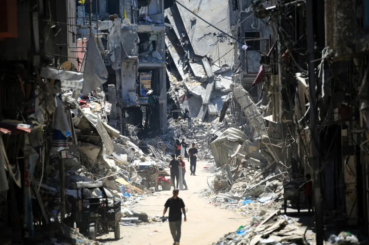 Hombres palestinos caminan por una calle estrecha pasando por edificios destruidos en Khan Yunis, en el sur de la Franja de Gaza, el 11 de junio de 2024, en medio del conflicto en curso entre Israel y el grupo militante palestino Hamas.