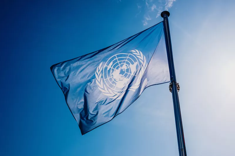 UN flag waved against the sun and blue sky.