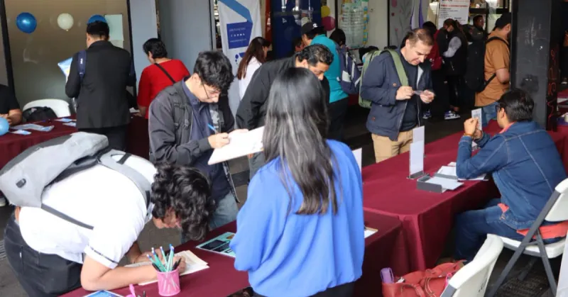Un total de nueve jóvenes en una mesa roja llenando ofertas de empleo, una persona está sentada y con un papel en mano.jpg