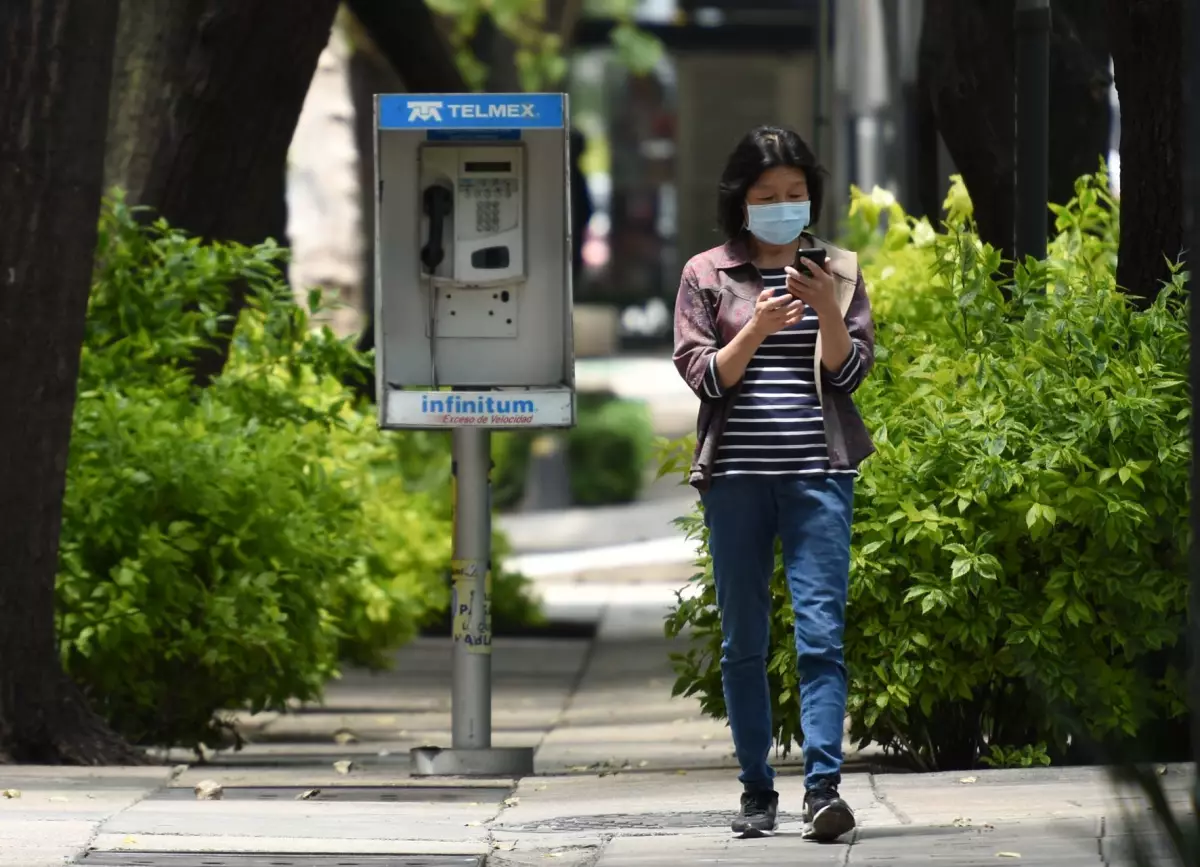 Una mujer utiliza su celular mientras pasa a lado de un teléfono público.