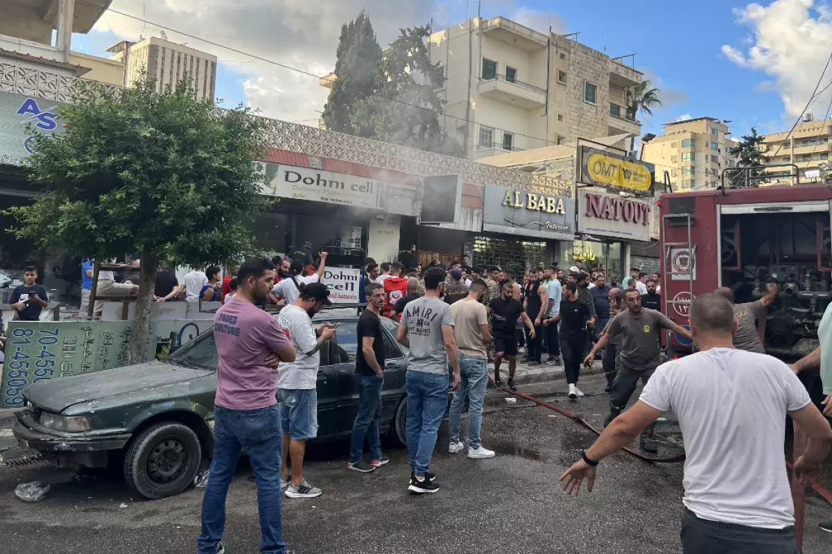La gente se reúne mientras los bomberos apagan las llamas en el lugar de una explosión de un dispositivo reportada en Saida, en el sur del Líbano, el 18 de septiembre de 2024.