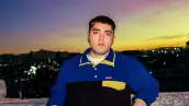 Foto de Kevin Kaarl recargado en una barda, lleva playera de manga larga y se ve el atardecer detrás.