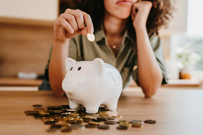 Worried young woman saving last coins in piggy bank