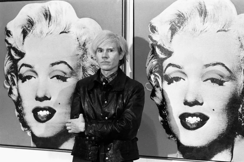 Andy Warhol frente a una de sus obras icónicas del arte pop.