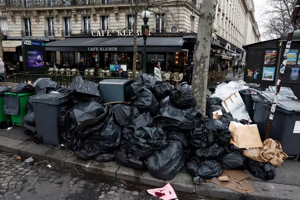 Gente camina en la calle donde los botes de basura están rebasados y la basura no ha sido recolectadas