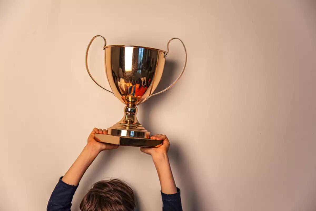 Champion cup in hands of kid on beige background