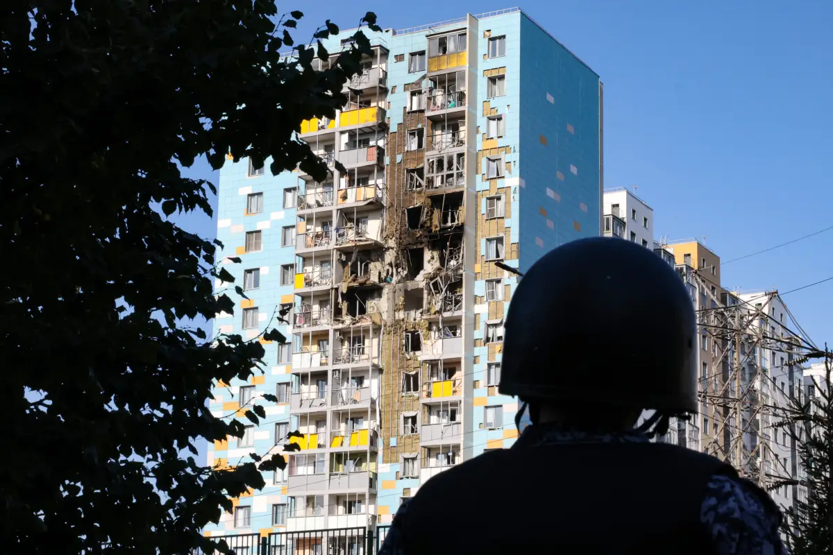 Un dron arrazó con una unidad residencial en Ucrania, en la iamgen es visible al fondo y centro un edificio de unos 14 pisos con graves destrozos y la sobra de la espalda de un oficial de control de daños a la derecha