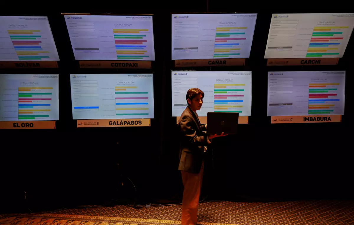 Un periodista mira su computadora portátil frente a una pantalla que muestra los resultados preliminares de un referéndum sobre medidas de seguridad para luchar contra la creciente violencia, en el Centro de Mando del Consejo Nacional Electoral en Quito, Ecuador, el 21 de abril de 2024.
