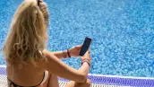 Mature woman sitting on the side the pool and texting by the pool