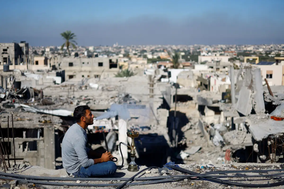 Un hombre palestino fuma shisha mientras observa las casas destruidas en ataques israelíes durante el conflicto, en medio de la tregua temporal entre Israel y el grupo islamista palestino Hamas, en el campo de refugiados de Khan Younis, en el sur de la Franja de Gaza, el 29 de noviembre de 2023.