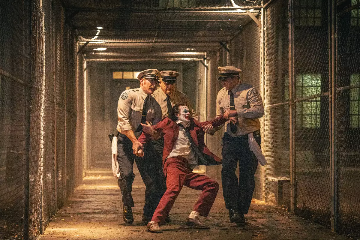 Foto de una escena de Joker 2 con tres policías arrastrando por un pasillo de una prisión al Guasón.