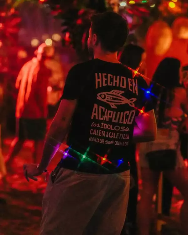 joven de espalda con una playera que dice "Hecho en acapulco" en un fondo iluminado de rojo.