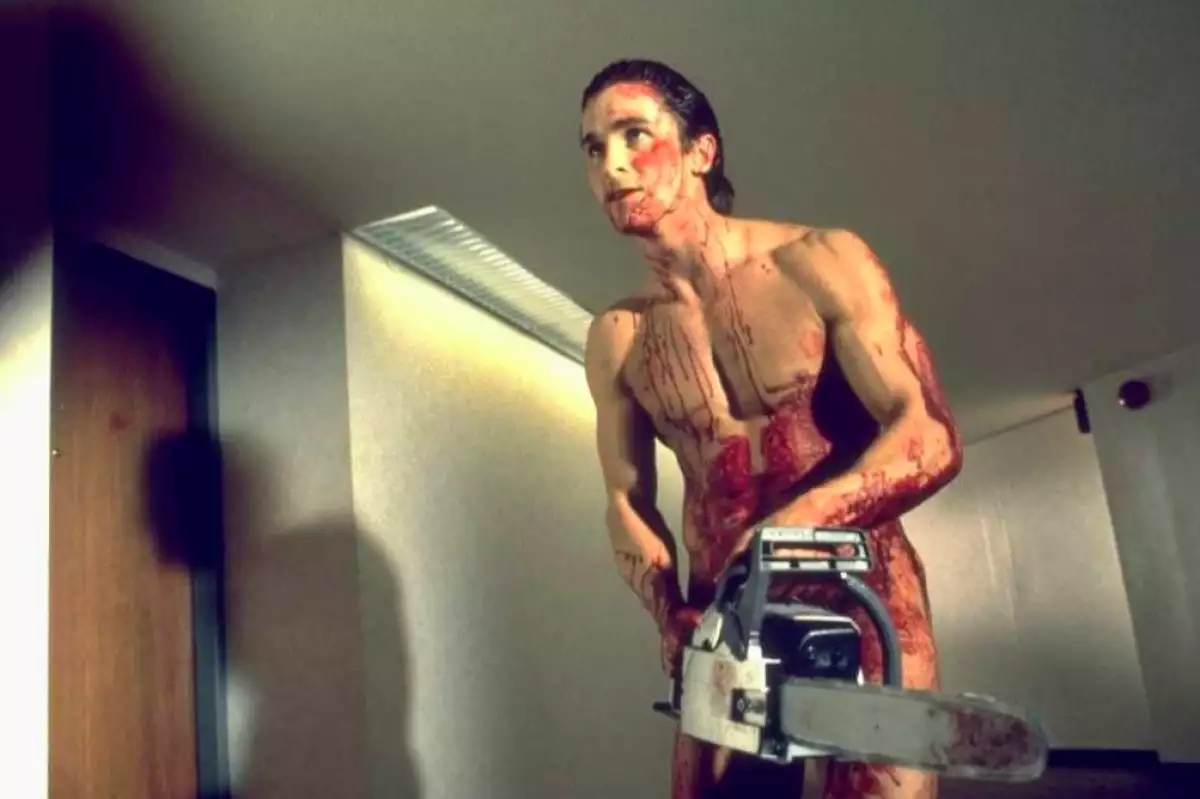 Foto de Christian Bale como Patrick Bateman desnudo y cubierto de sangre con una sierra eléctrica en las manos en la película American Psycho.