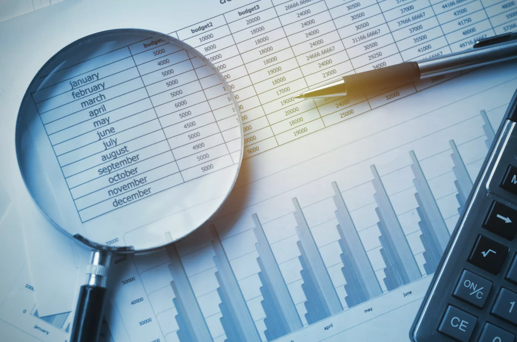 Se observa una hoja con datos numéricos, una calculadora, un lapicero y una lupa.