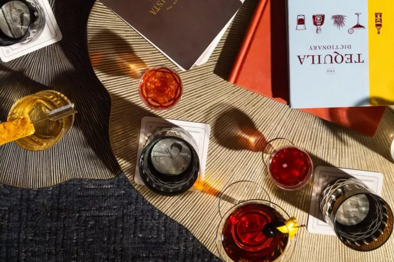 Foto de una mesa vista desde arriba del bar Jewel of the South en Nueva Orleans con siete vasos servidos con distintos cocteles y dos libros sobre mixología