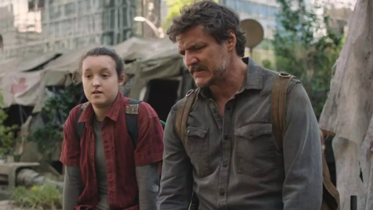 Foto de una escena de The Last Of Us con Ellie (Bella Ramsey) y Joel (Pedro Pascal) sentados lado a lado con una ciudad en ruinas detrás de ambas.