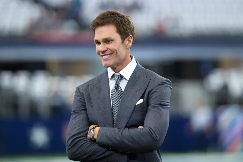 Foto de Tom Brady con los brazos cruzados y vistiendo un traje y corbata.