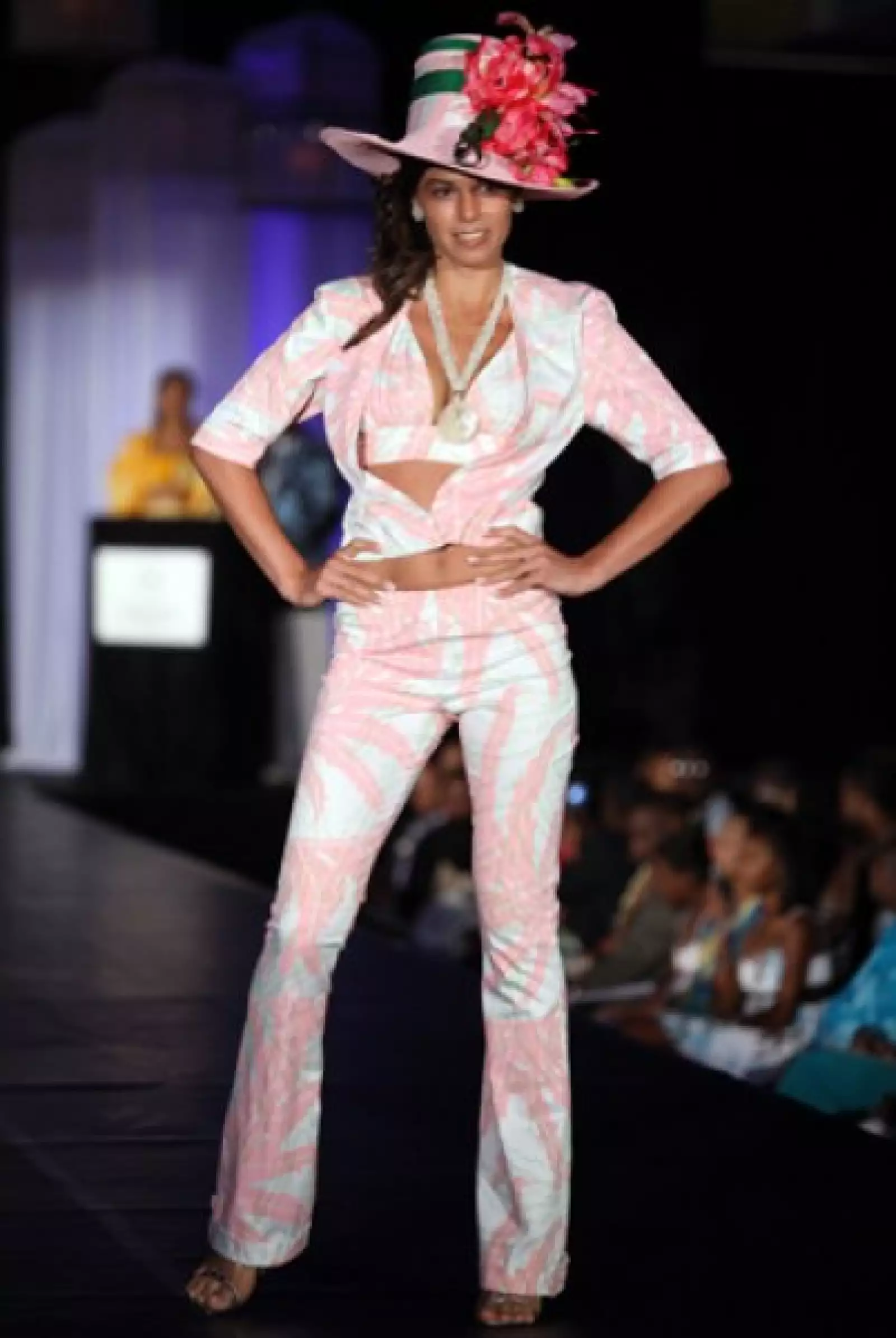 Dragana Atlija, de Serbia, en un conjunto de pantalón, saco y un sexy top, todo en rosa y blanco. El sombrero de copa alta adornado además con grandes flores.