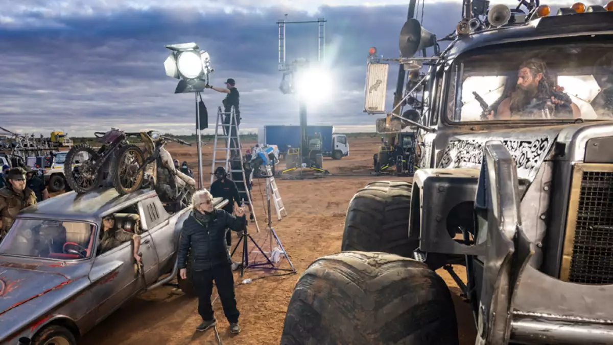 Al centro de la foto, George Miller en el set de grabacion de Furiosa, a la izquierda Anya Taylor-Joy sobre un auto y a la derecha Chris Hemsworth sobre un trailer.
