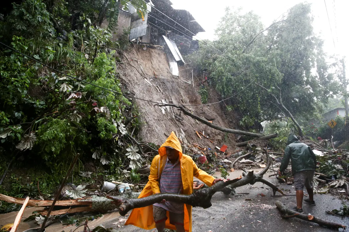 Residentes limpian un derrumbe en un camino mientras la tormenta tropical Julia golpea con viendo y lluvia en San Salvador, El Salvador. 