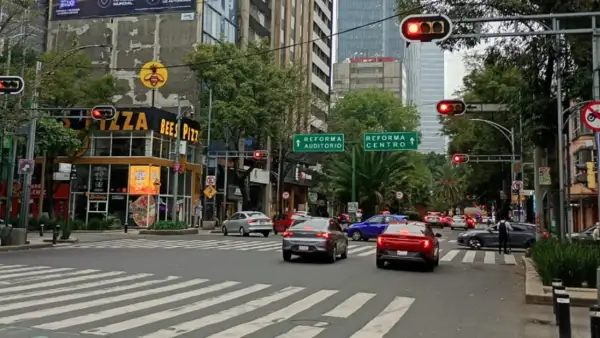 Dos carros circulan sobre una avenida de la CDMX. Hay semáforos y en la esquina del lado izquierdo hay una pizzeria.jpg