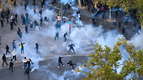Grupos de jóvenes en medio de gases lacrimógenos en una plaza donde hay árboles.jpg