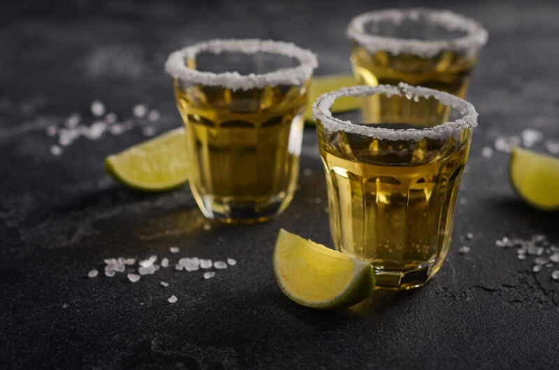 Gold tequila with lime and salt rim on dark stone or concrete background.