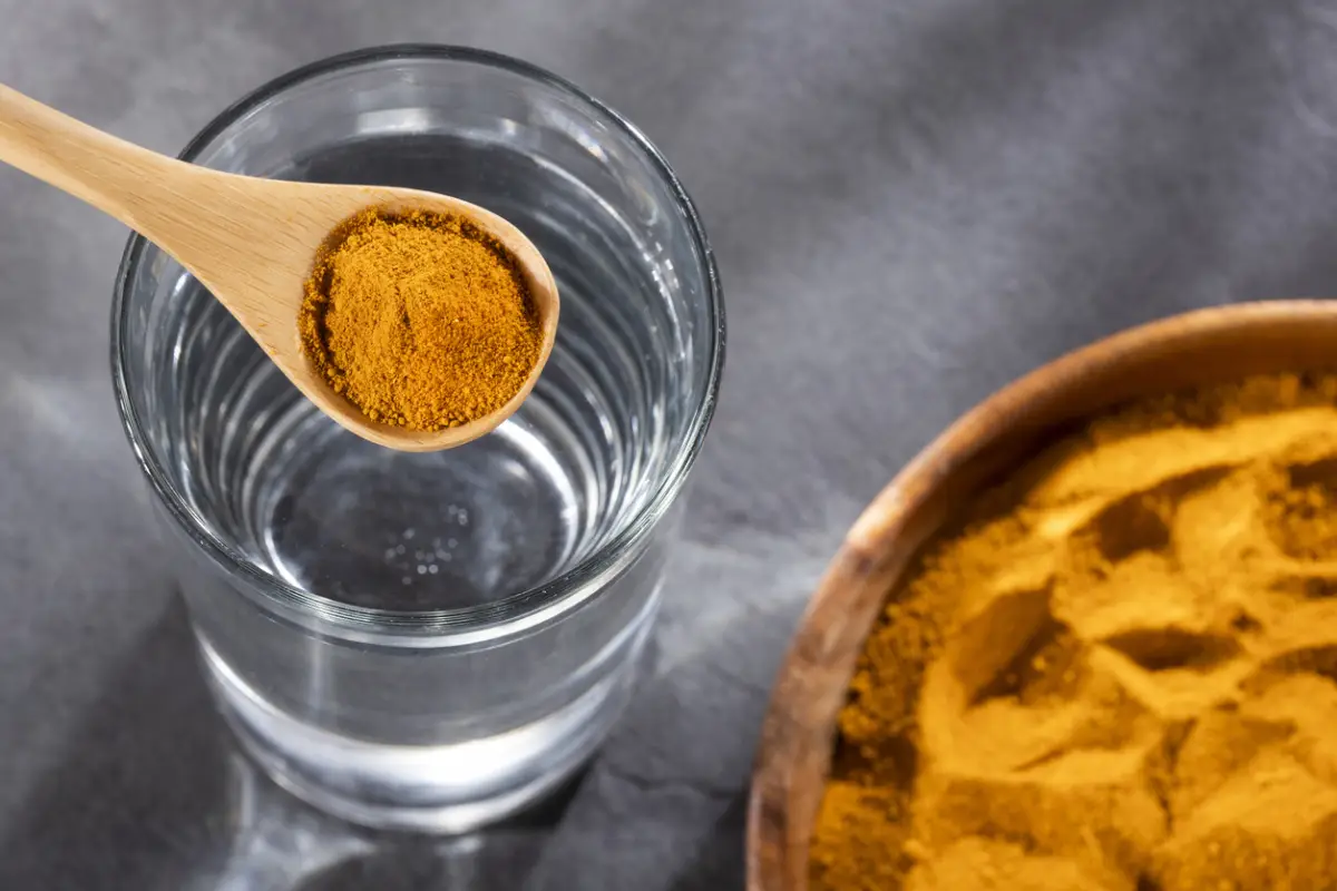 Spoon with organic turmeric and glass of filtered water