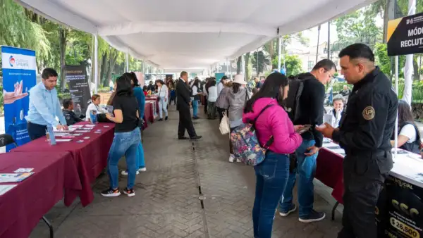 Un pasillo largo al aire libre con mesas al lado y mujeres y hombres hablando, traen folletos en la mano .jpg