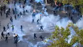 Grupos de jóvenes en medio de gases lacrimógenos en una plaza donde hay árboles.jpg