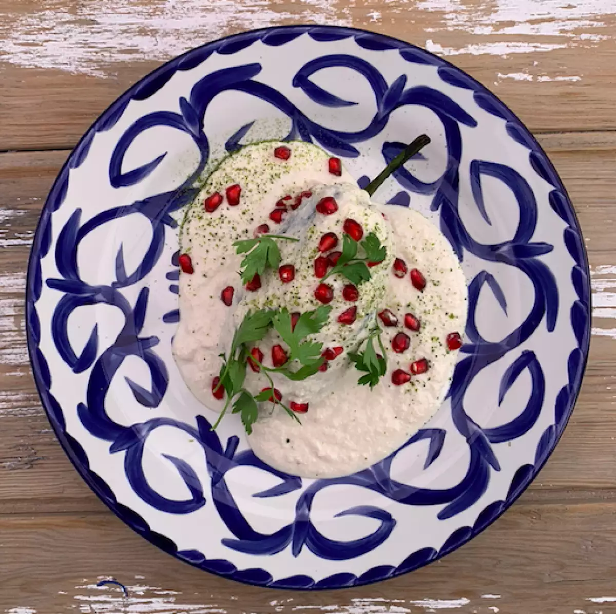 Foto de chile en nogada servido con la salsa (nogada) encima y granos de granada roja.
