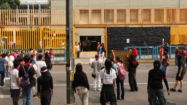 Grupo de jóvenes de espaldas frente a unas rejas amarillas de un plantel de la UNAM.jpg